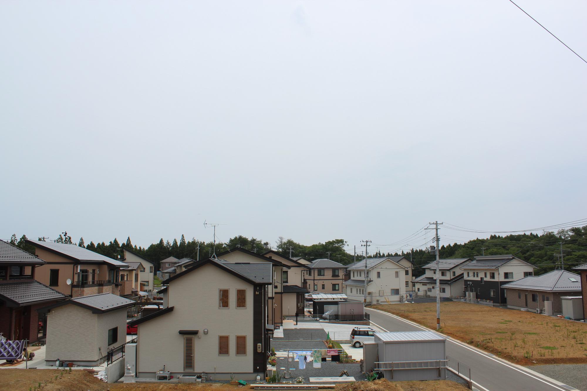 新しく整備された住宅地で、複数の一戸建て住宅が整然と並び、舗装された道路と電柱が整備された静かな郊外の町並みの写真