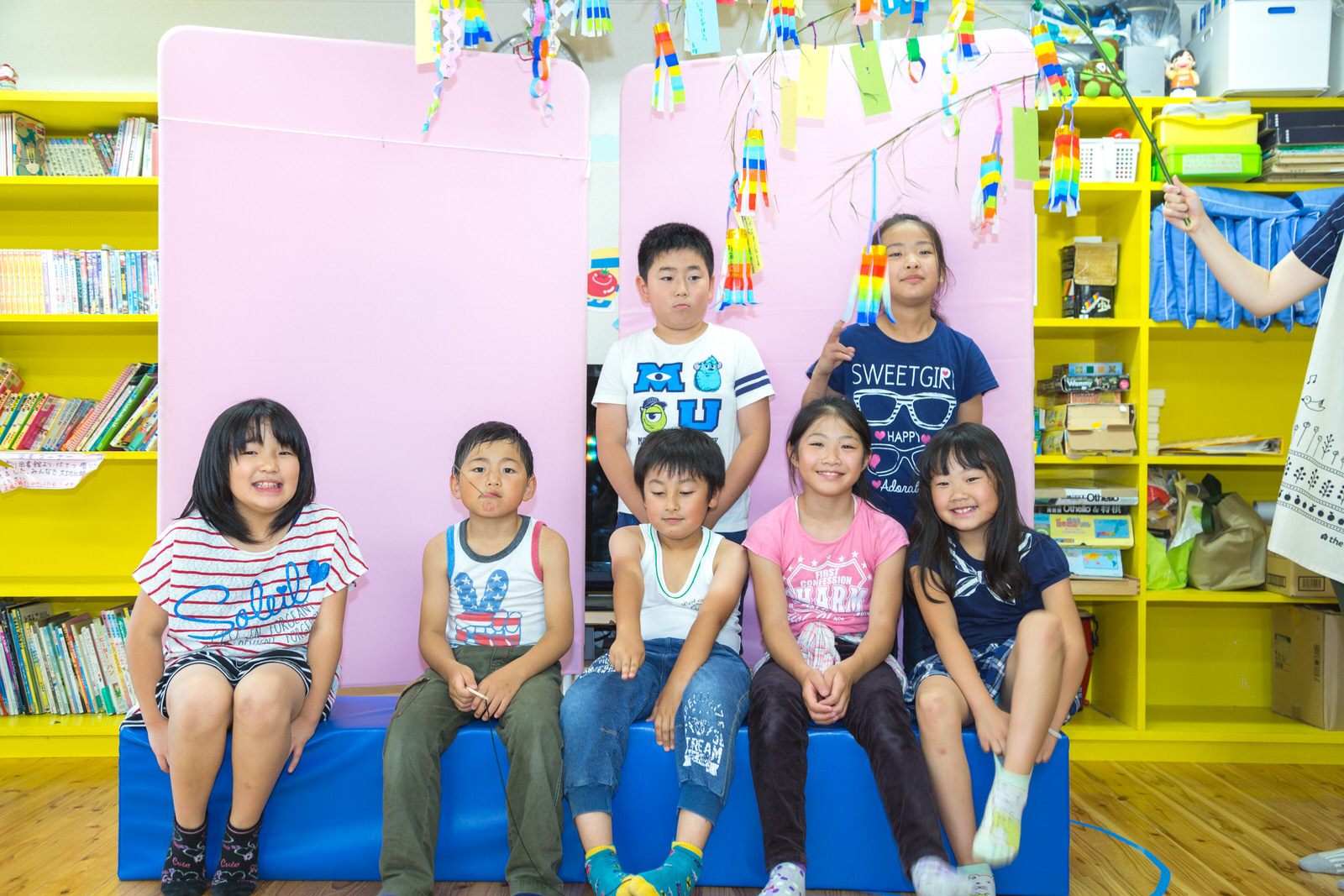 七夕飾りがされた笹の枝の下で、前列の5人が長椅子に座り、後ろの2人が立っている集合写真