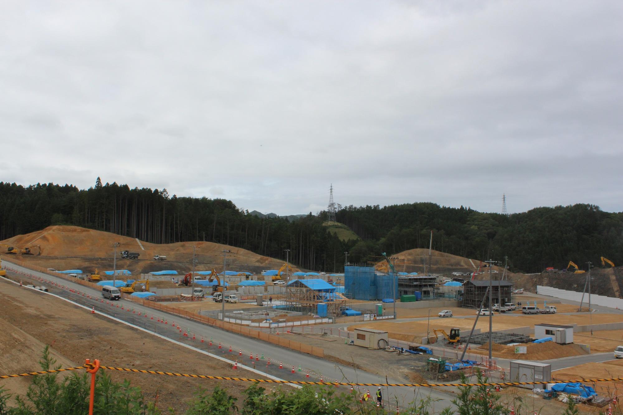 起伏が整えられた造成地の手前にアスファルト舗装された道路ができ、住宅地のの基礎工事が進められている写真