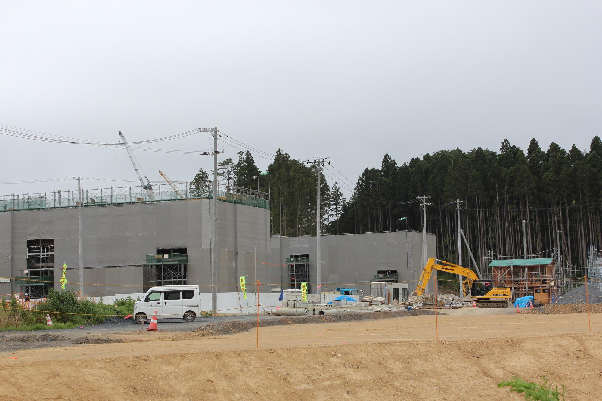 災害公営志津川中央住宅の周りに足場が組まれ、建物奥には2台のクレーン、横には1台のショベルカーが稼働している様子の工事現場の写真