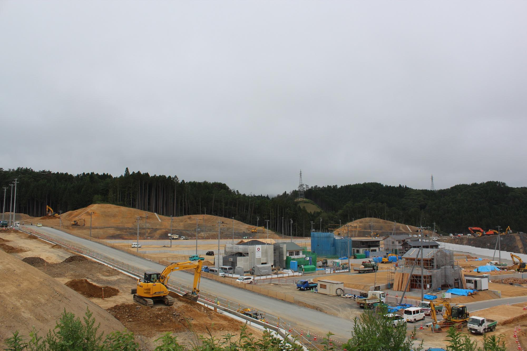 造成がほぼ完了し、整地された広い住宅地予定地に舗装道路や側溝が整い、背景に住宅の基礎工事が進む様子が写された写真