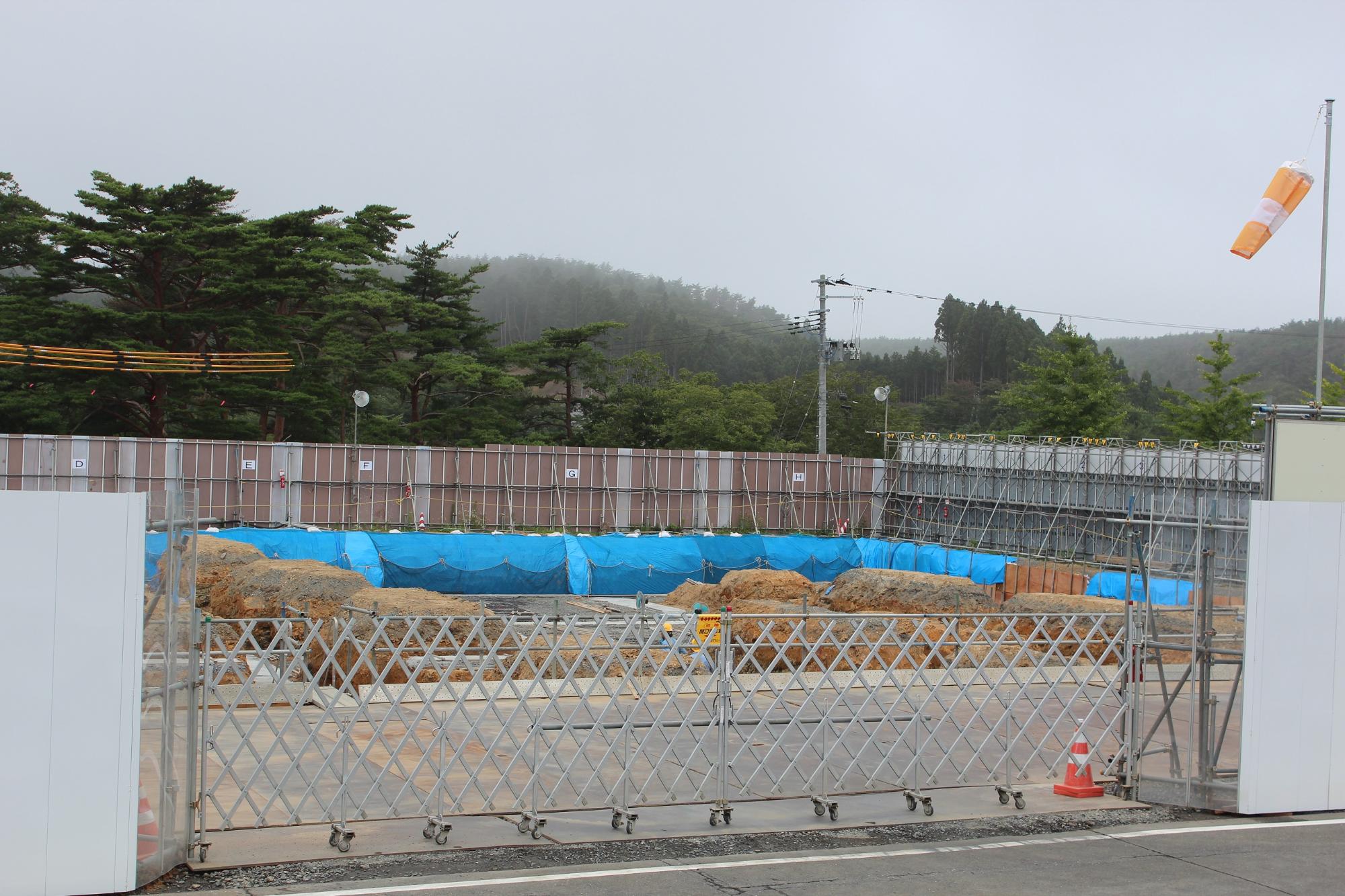 ブルーシートで覆われた基礎工事中の建設現場と山林が見える写真