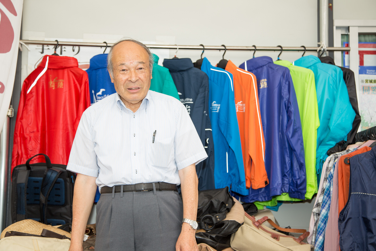 色とりどりのジャンバーが掛けられた壁の前に立つ千葉さんの写真