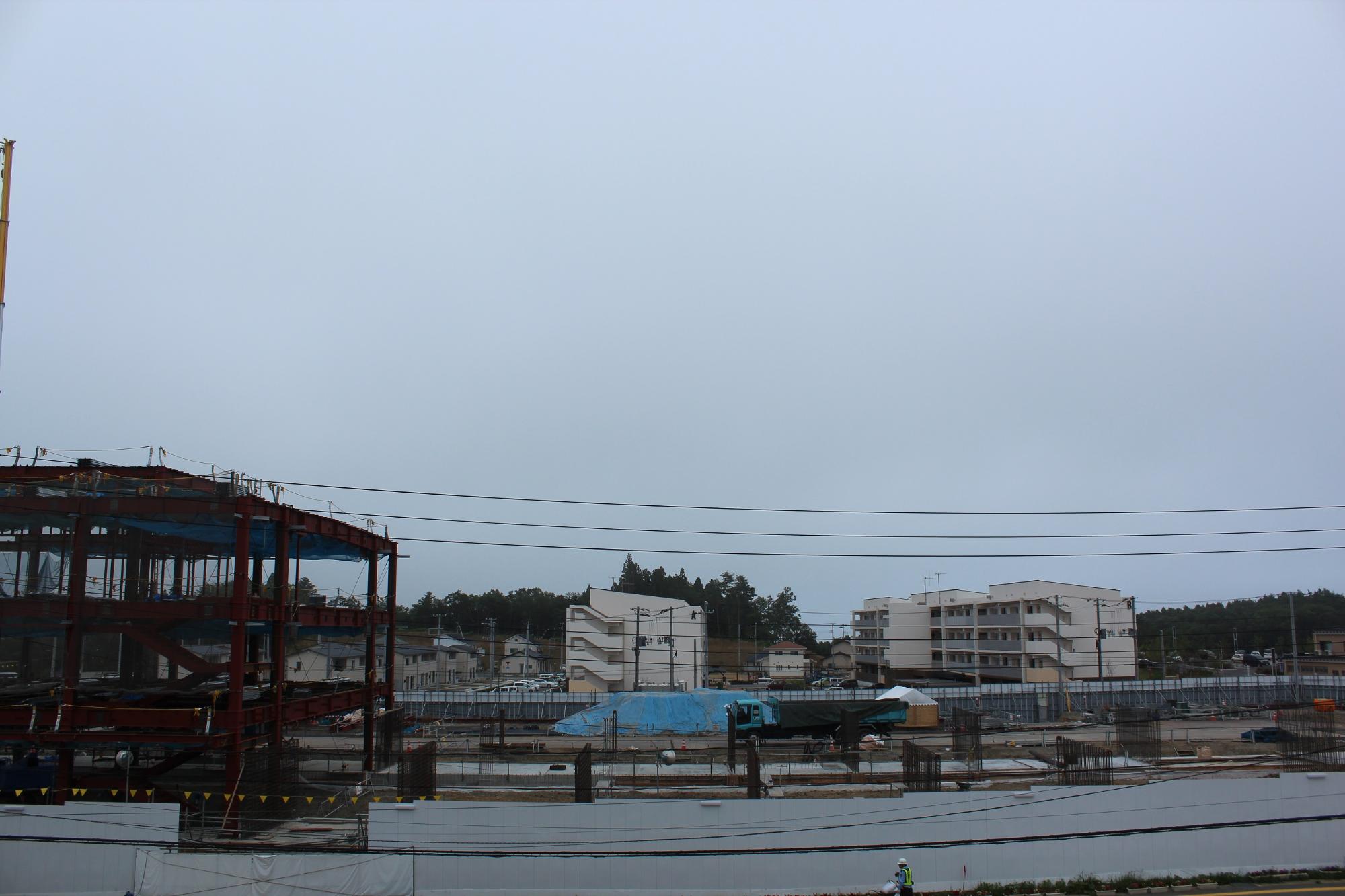 建設中の鉄骨がむき出しになったビルと、その背後に複数の集合住宅や送電線が見える平成28年8月2日現在の写真