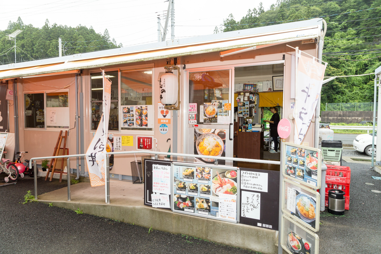 店の入り口や、入り口前のスロープにたくさんのメニューポスターが貼られた、仮設店舗の外観写真