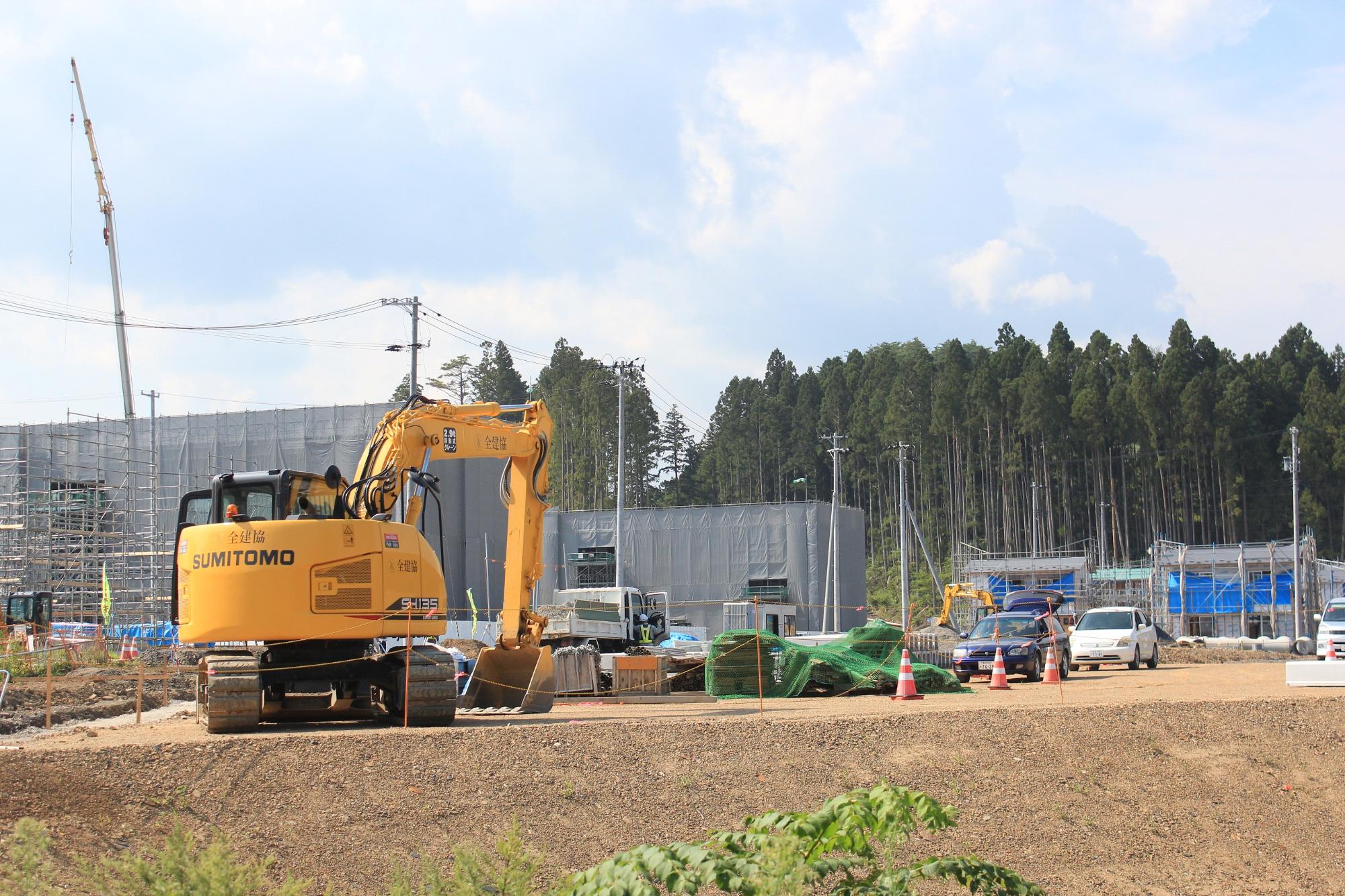 足場が組まれた災害公営志津川中央住宅の横に黄色い大きなショベルカーが停まっている写真