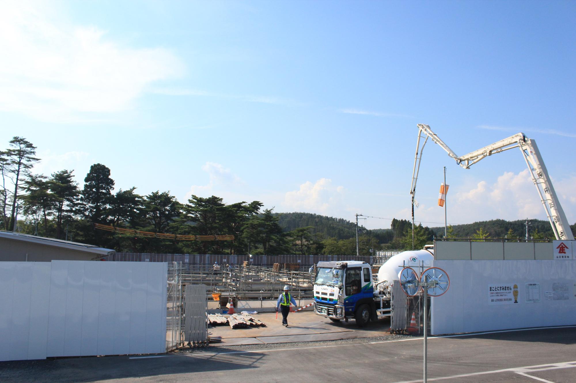 工事現場入り口付近に停車したコンクリートポンプ車と作業員がいる建設途中の現場の写真
