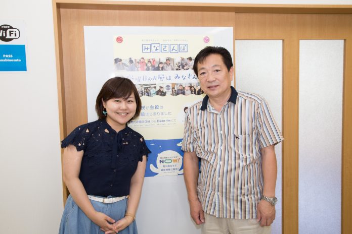 みなさんぽのポスターが貼られたドアの前に並んで立っている小坂さんと女性リポーターの写真