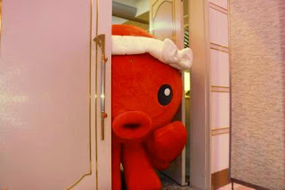 赤いタコのオクトパス君の着ぐるみキャラクターが、会場のドアの隙間から顔を出して入ってこようとしている可愛らしい瞬間の写真
