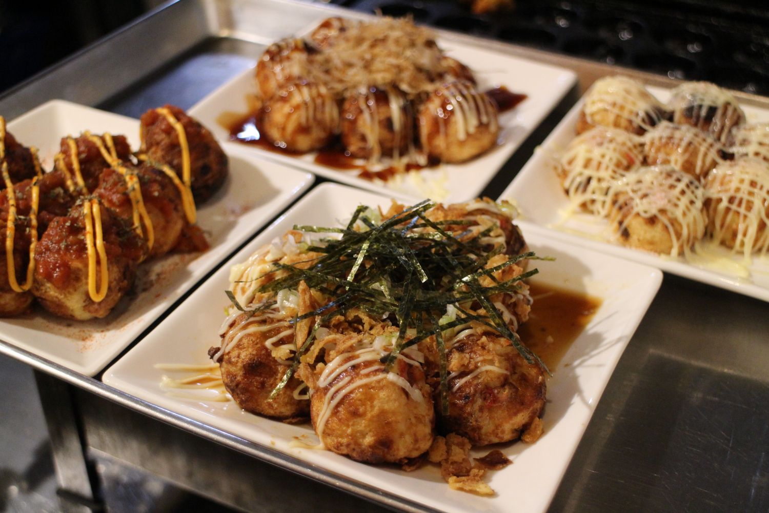 さまざまなトッピングが施された4種類のタコ焼きが白い皿に美しく盛られている様子の写真