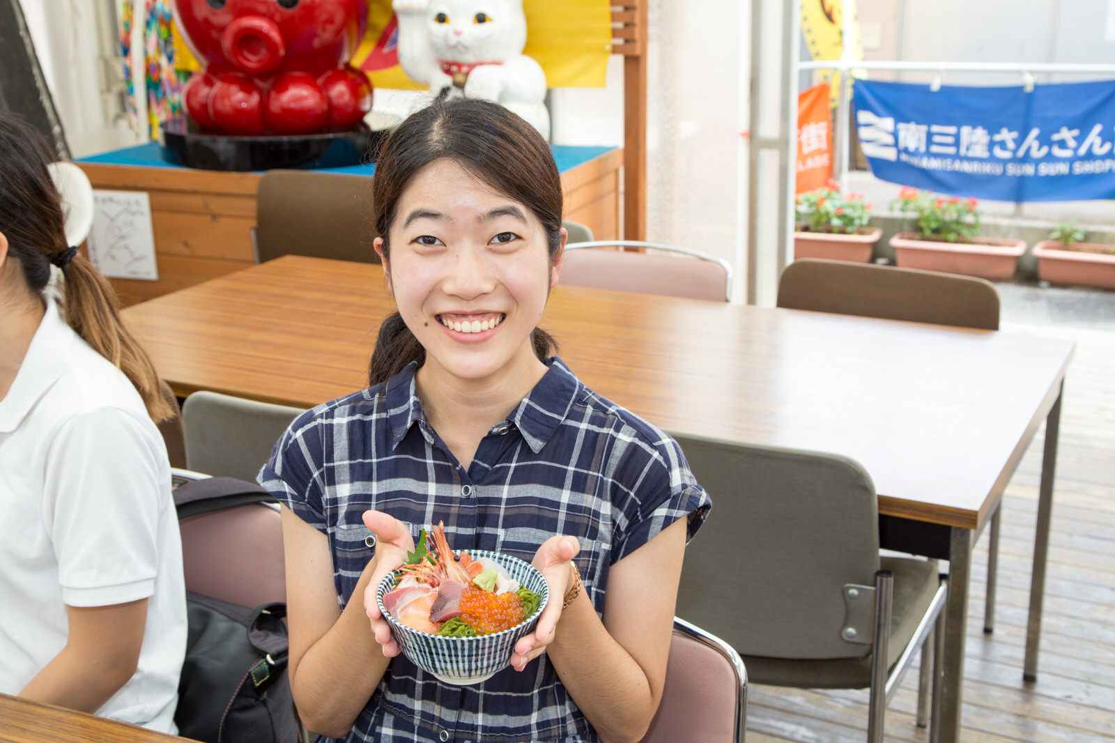 えびやイクラ、刺身などが乗った海鮮丼を両手で持って笑顔の女性の写真
