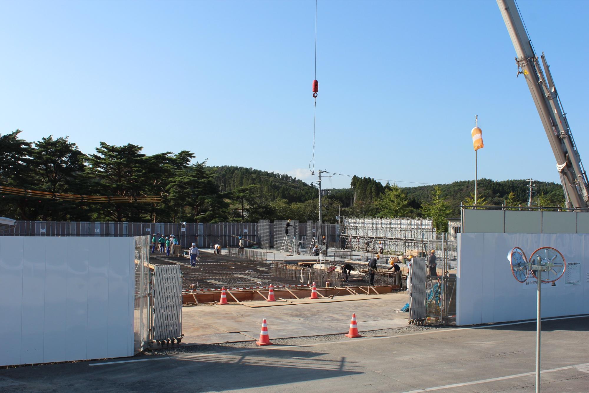 大きなクレーン車が稼働している建設現場で多くの作業員が基礎鉄筋の組み立てをしている初期段階の写真