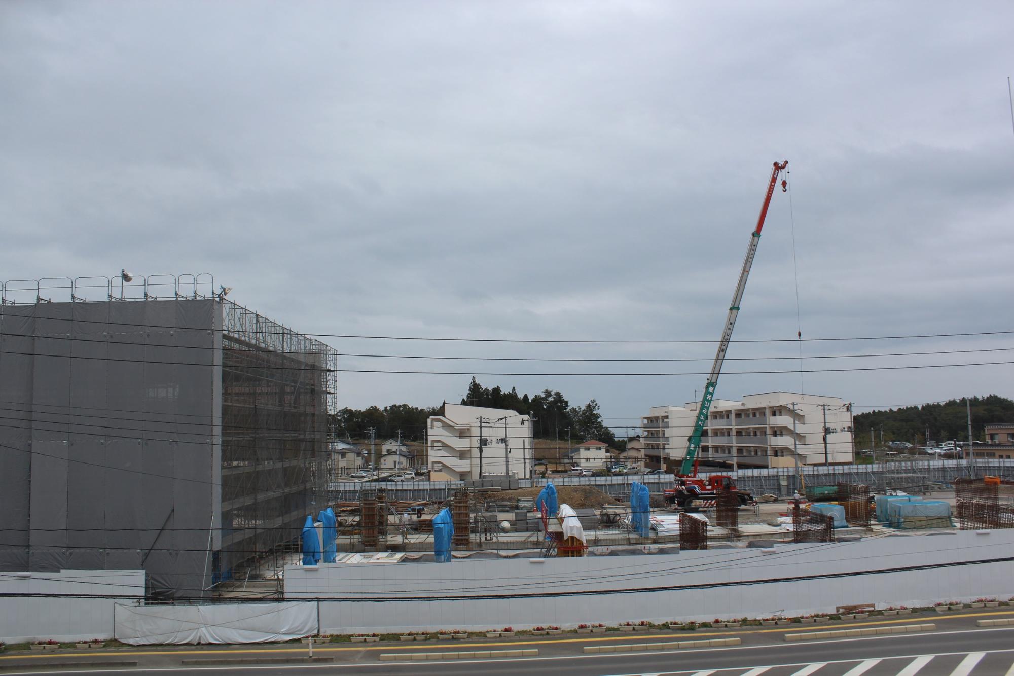 大きなクレーンが稼働する建設現場に防護シートに覆われた建物が見える平成28年10月4日現在の写真