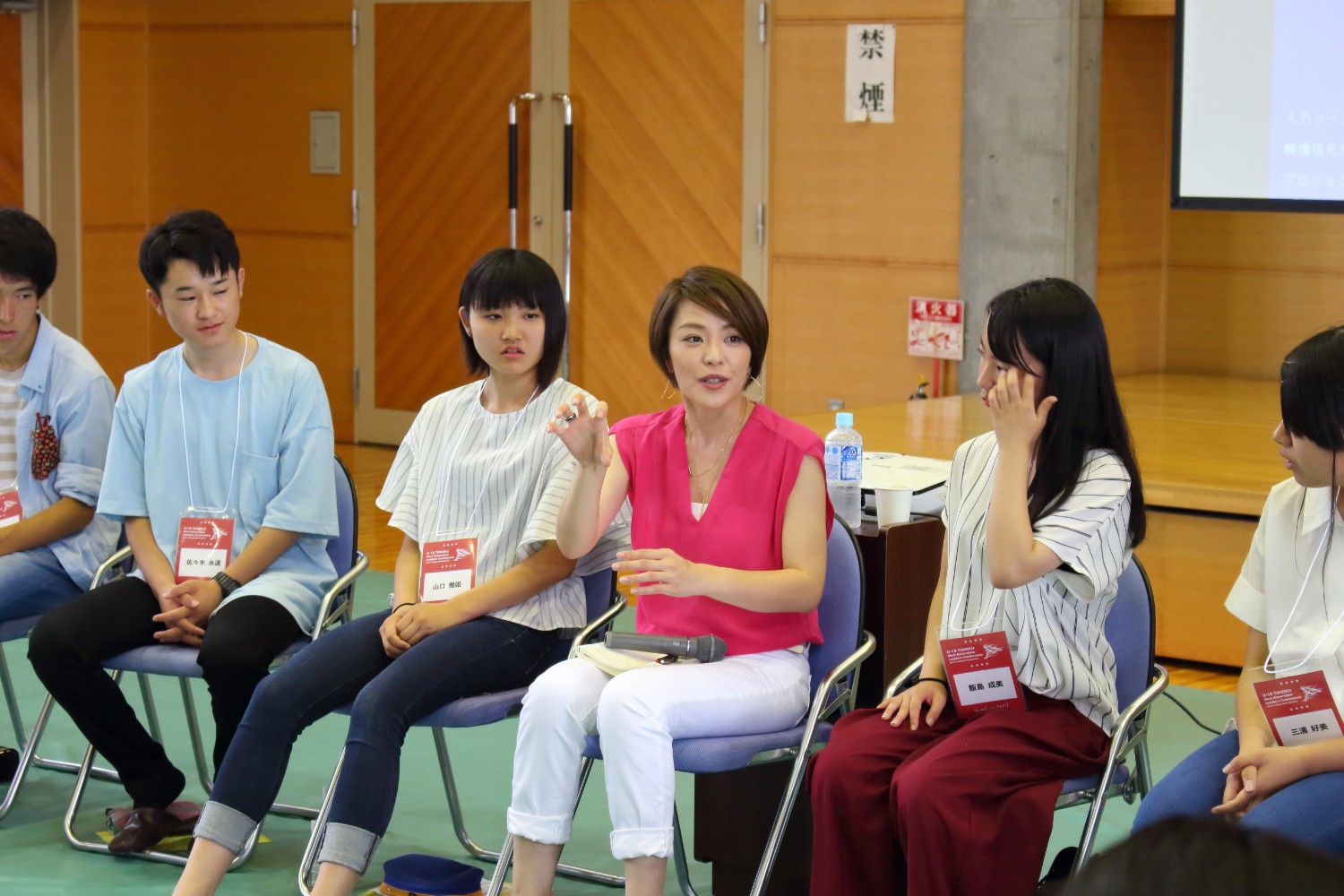 円形に並べた椅子に高校生数人が座っており、生徒の間に座っているピンクの服を着た今井議員が手振りを交えて熱心に話している様子の写真