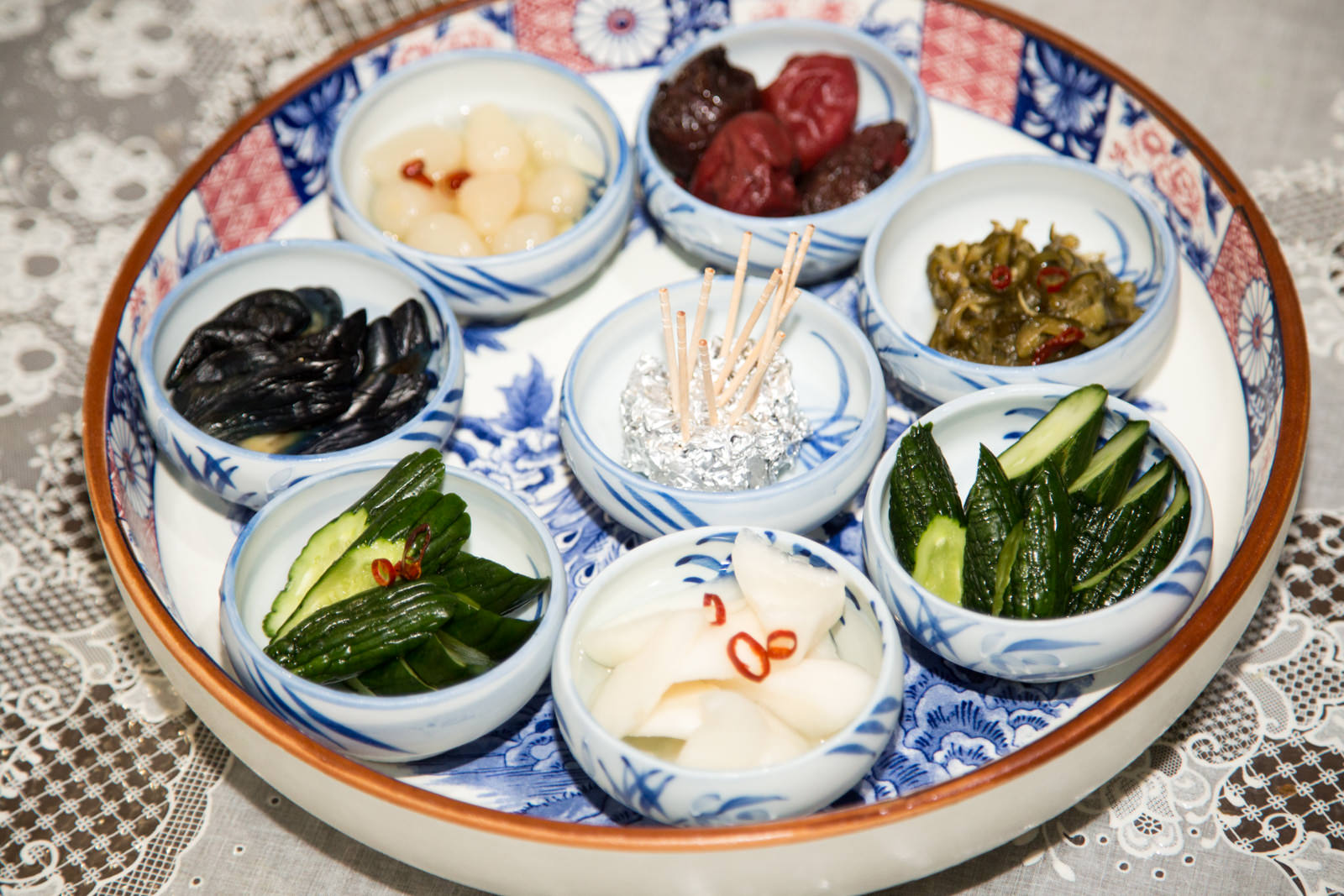 中央に楊枝を立てられていて、周りに色とりどりの漬物が7つの小鉢に分けて盛られている写真