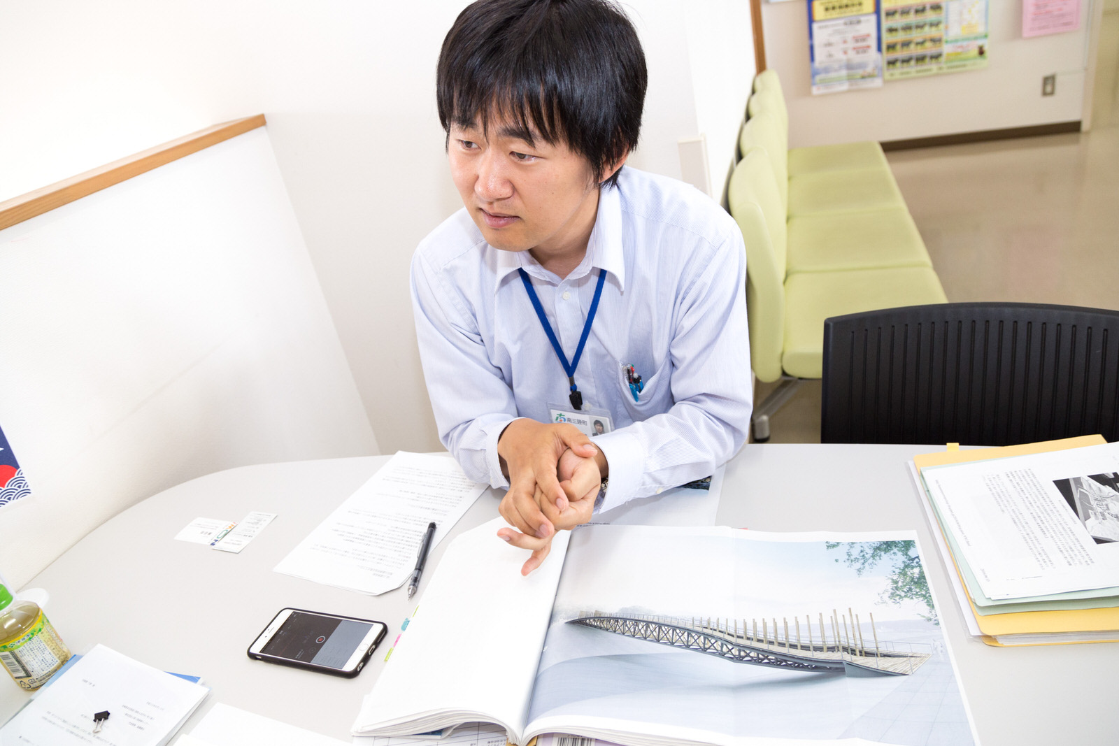 たくさんの資料を広げた白いテーブルの上に、両掌を重ねて取材に対応する佐藤俊介さんの写真