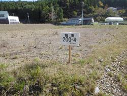 空き地に「城場200-4」と番号が書かれた白い立て看板が立っている写真