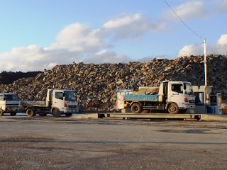 大型車両が列を作って並んでおり、先頭の車が計量器の上に乗って重さを量っている様子の写真