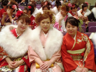 3人の艶やかな振袖姿の新成人が並んで椅子に座っており、中央には白いショールを肩にかけたピンク色の振袖姿の関内望未（みいわ）さんが写っている写真