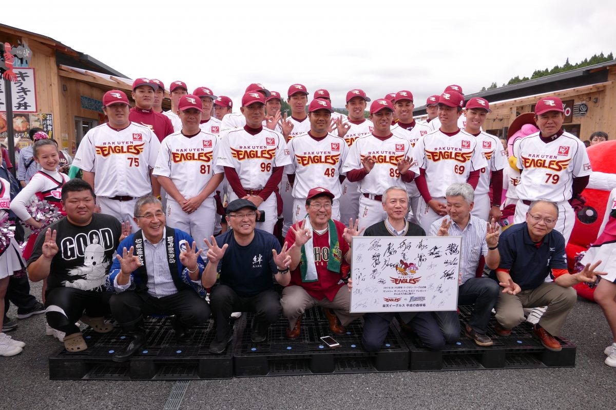 楽天イーグルスのユニフォームを着た選手たちと、地元住民や関係者が集合して記念撮影をしている、地域交流イベントの様子を収めた写真