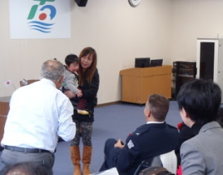 前方に立つ子どもを抱えた女性に、関係者の男性が声をかけている様子を写した写真