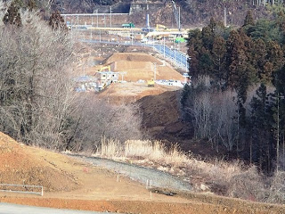 手前には木が覆われ、その奥に見える建設現場を遠目に写した写真