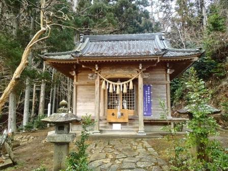 石灯籠と小道が続く先に、注連縄が飾られた木造の社殿が森の中に建っている写真