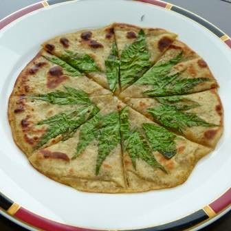 赤と黒の縁の白い丸皿に、トウキリーフの葉が置かれた8等分にカットされたピザが盛り付けられた写真