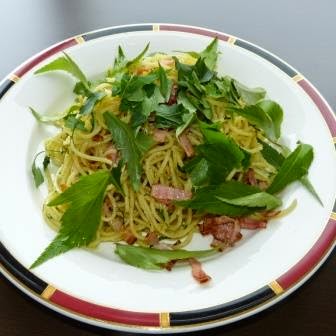 赤と黒の縁の白い丸皿に、トウキリーフやベーコンなどの材料で作られたパスタが盛り付けられた写真