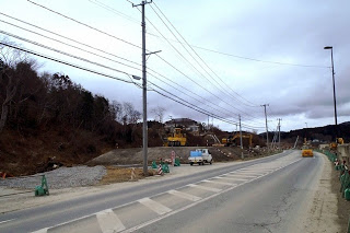 舗装された道路の脇で工事が行われており、重機や作業用車両が並んでいる写真