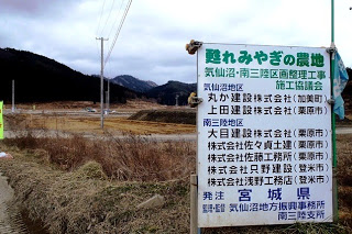 農地の造成工事に関する看板が立てられ、背景には山と未整備の畑が広がっている写真