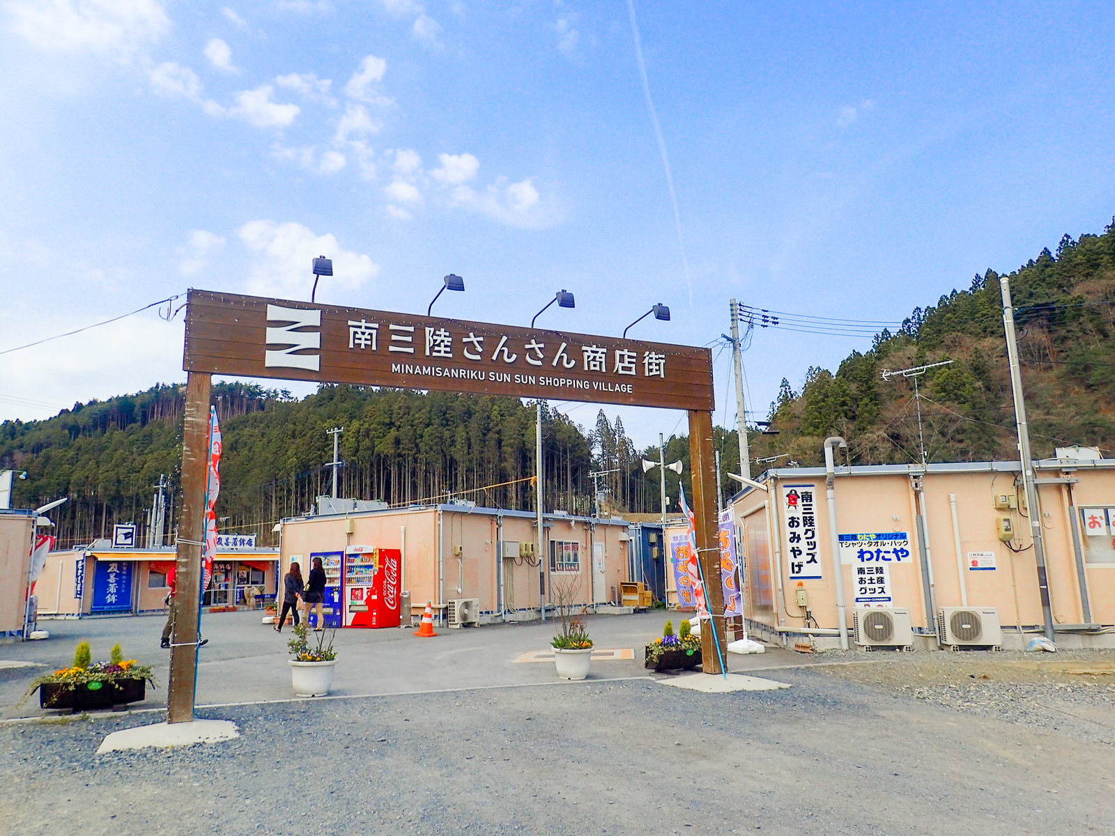 「南三陸さんさん商店街」と白い文字で書かれた、大きな茶色のゲートの中に仮設商店街の建物が建っている写真