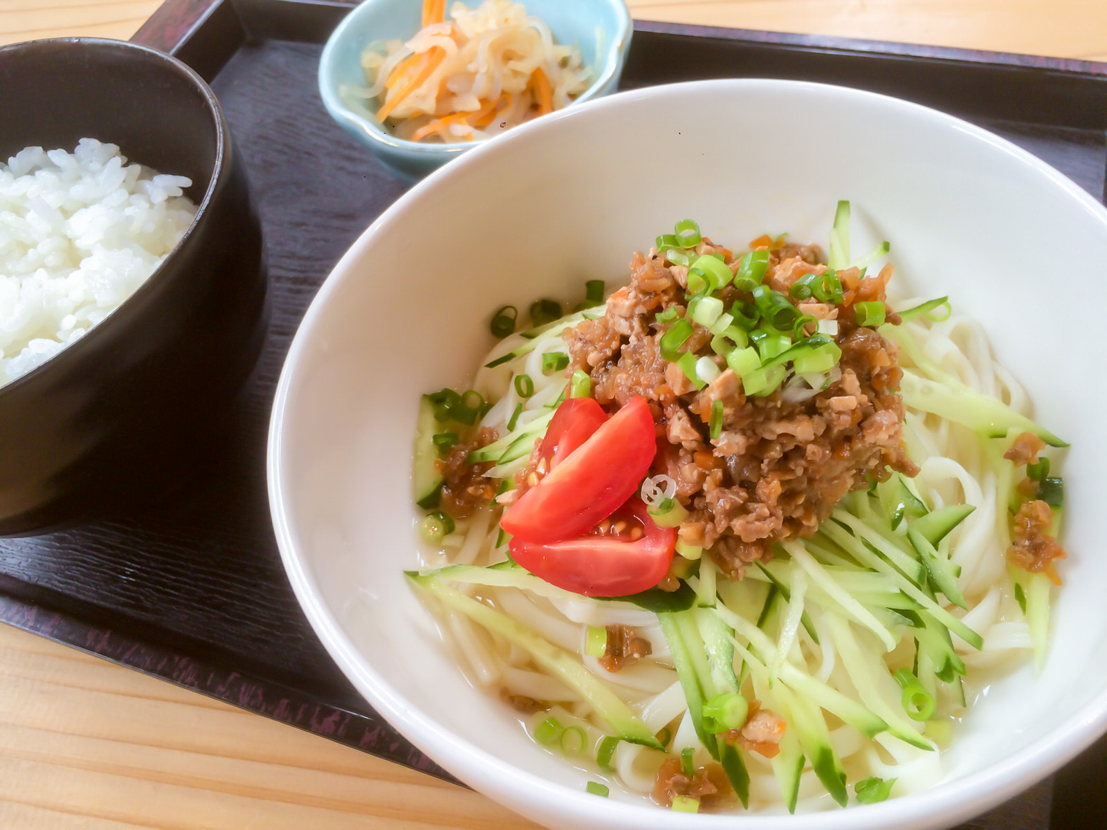 白い器に白い細麺の上に刻みきゅうり、トマト、ひき肉が盛られた台湾風ジャジャ麺と、小鉢、ご飯が黒い四角いお盆に乗っている写真