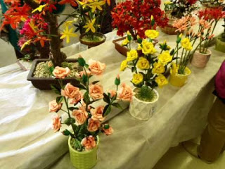 白い布がかけられた長机の上にピンクや黄色、赤のシルクフラワーが鉢に活けられて並んでいる写真