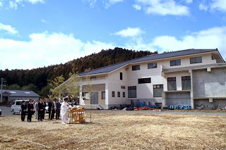 奥に建物が見え、その前の平地で安全祈願祭が行われている写真