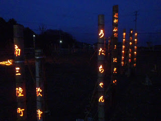 暗闇の中、並んで立てられた竹灯籠に刻まれた「南三陸町」や「うたちゃん」などの文字が橙色の光で浮かび上がっている写真
