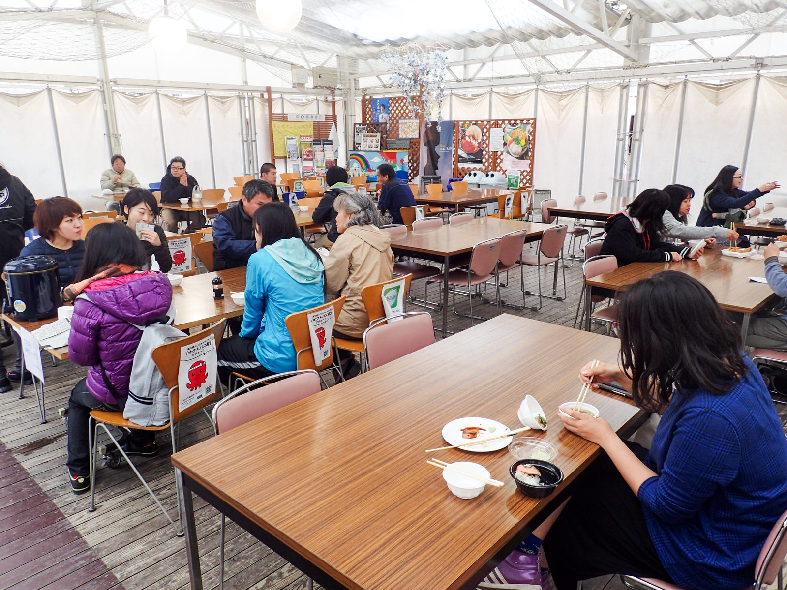 広いテントの中にたくさんのテーブルとイスが置かれ、席に座った人々が購入したものを食べたりしている様子の写真