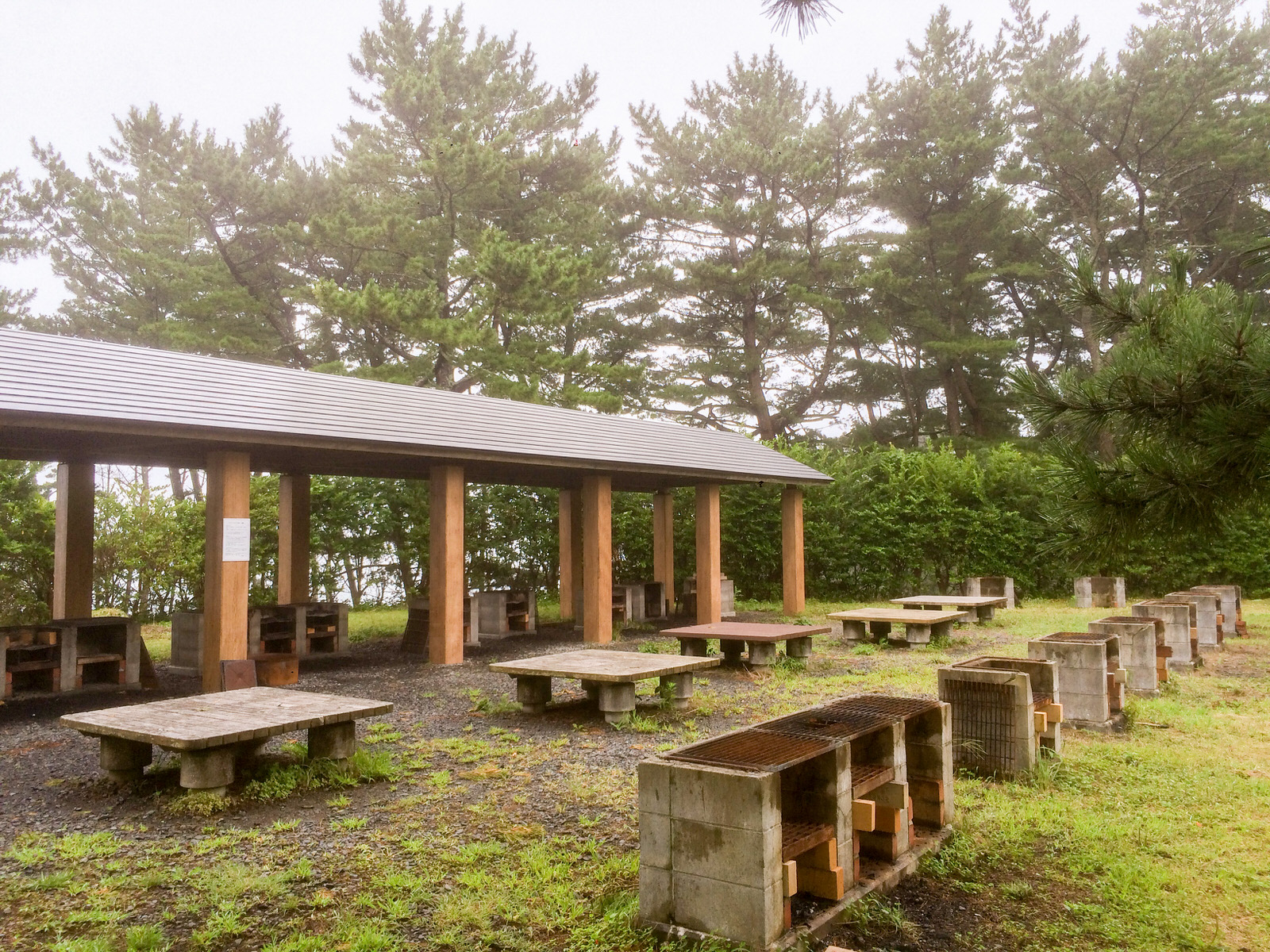 木々に囲まれた場所に、屋根付きの調理場と複数のかまどやテーブルが整然と並ぶバーベキュー広場の写真