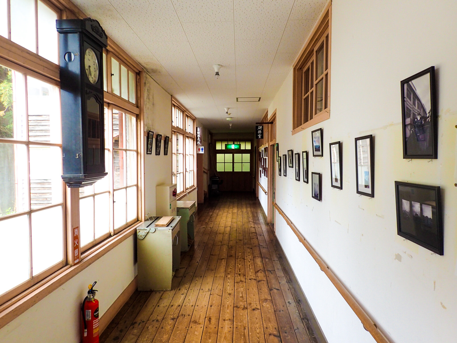木造校舎の廊下に額に入った写真や古い掛け時計が飾られている写真