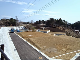 電柱や舗装道路、建設用の機械が確認できる、傾斜地を活かして段差のある区画が整備されている写真