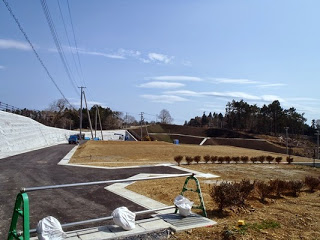 白い擁壁や舗装道路、整備された芝地に植栽がある新興住宅地の一角の写真