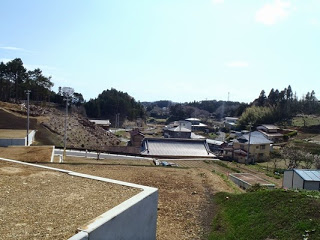 区画整備された高台の土地の下には、木々や田畑、既存の民家が点在する風景が広がる写真