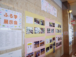 館内の壁に「ふる学展示会」と書かれたタイトルや手書きのポスター、写真付きの発表用紙が色画用紙に貼られて並んでいて、学習の成果が展示されている様子の写真