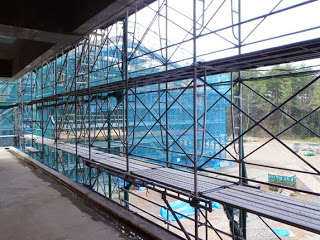 画像の左側には建物の内部が見え、右側には青いネットで覆われた足場が広がっている建設現場の写真