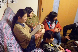 数人の若い女性たちがカバーがかけられたソファの上に並んで座り、一人は資料を見ながら、他の人は静かに話を聞いているミーティング中の写真