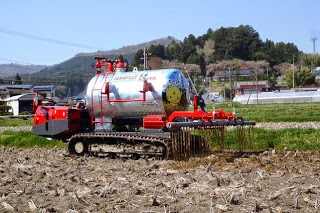 銀色のタンクから液肥を地面にまきながら進む、キャタピラ付き液肥専用散布車が畑の上を走行している写真