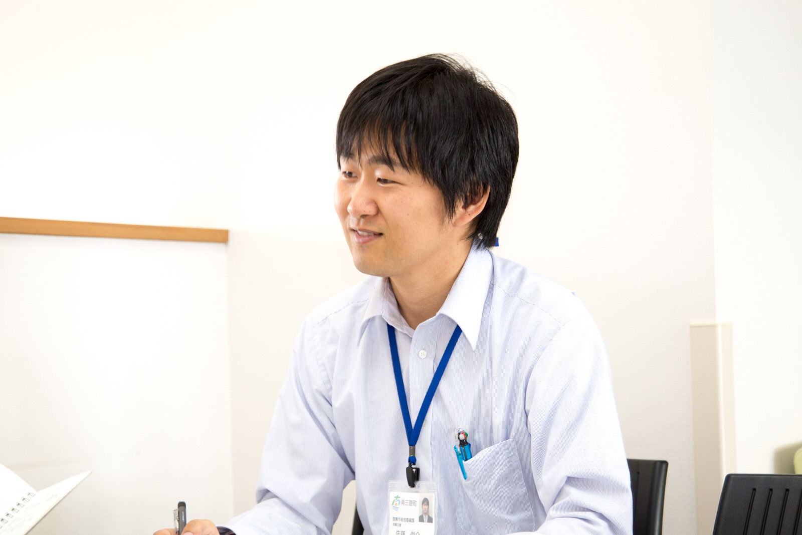 白い壁の室内で椅子に座り笑顔で質問に答える佐藤俊介さんの写真