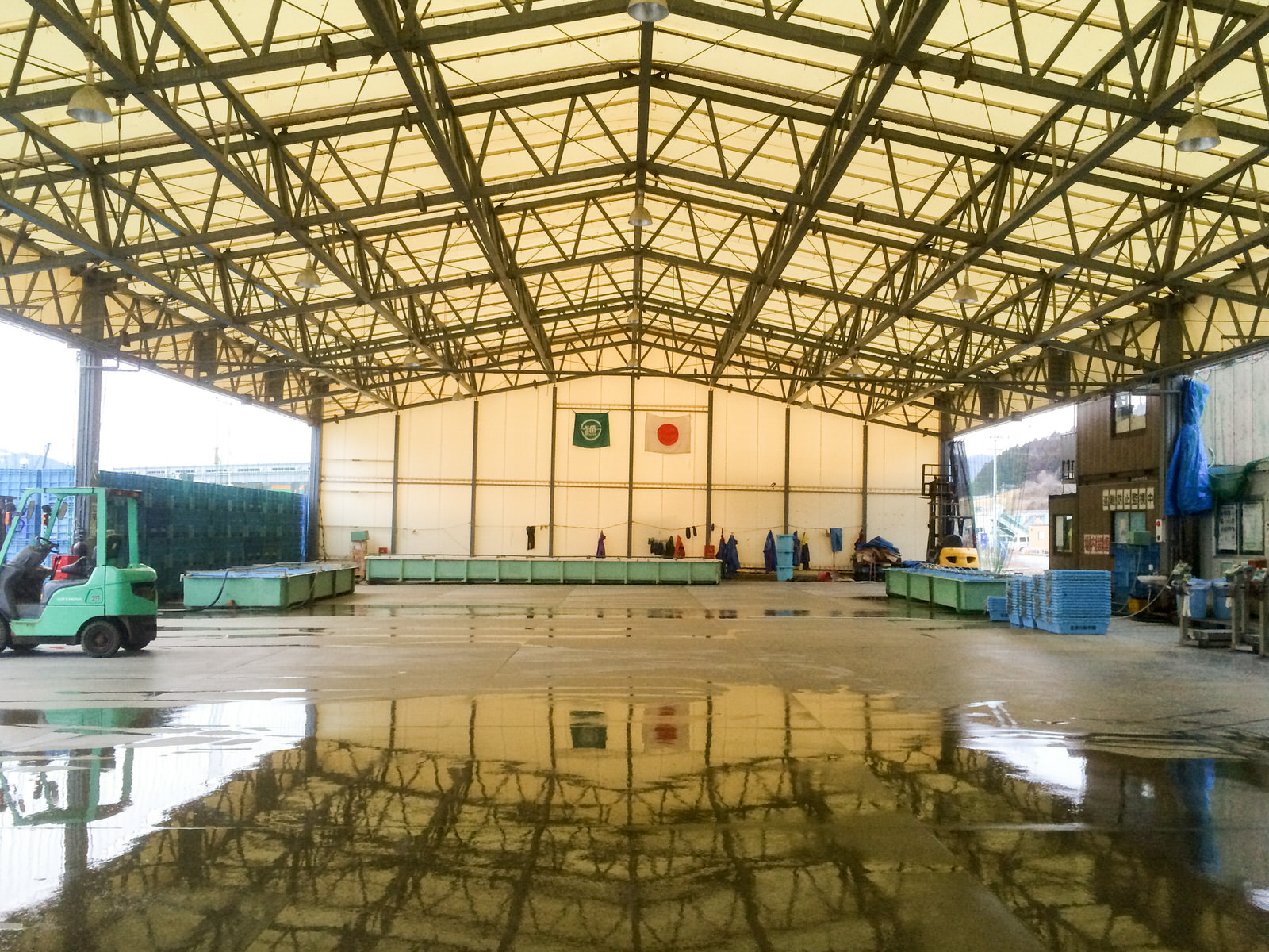 屋根付きの仮設市場に水色のパレットやコンテナが整然と置かれ、1台のフォークリフトが駐車してある市場内の写真