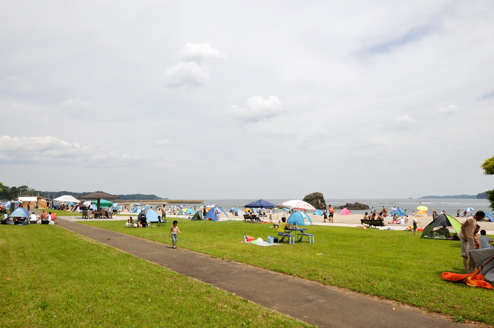 遊歩道の左右にある芝生広場とその先の砂浜に多くのテントが張られ、家族連れなどで賑わっている荒島パークの写真
