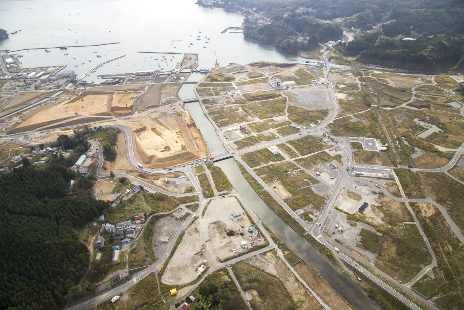 リアスの海へ続く川沿いの更地にたくさんの工事車両が点在し、道路が通り復興が進んでいる様子がわかる写真